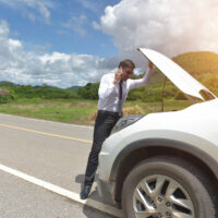 A young business man strained with his damaged car, looking frustrated at the engine failure.