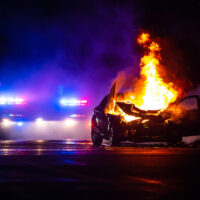 Car on fire at night with police lights in background