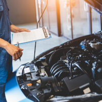 Car mechanic holding clipboard and checking to maintenance vehicle by customer claim order in auto repair shop garage. Engine repair service. People occupation and business job. Automobile technician