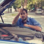 stressed man having trouble with broken car looking in frustration at failed engine