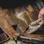 Hands of a man seen using a pair of pliers to remove old rusty metal from the car underbody. Restoration of a car and stubborn metal piece.