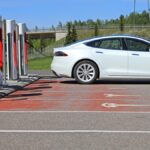 White Tesla Model S Electric Car Charging Battery at Tesla Supercharger station, side view.