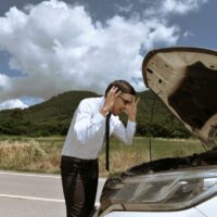 A young business man strained with his damaged car, looking frustrated at the engine failure.