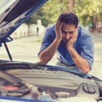 stressed man with broken car looking at failed engine