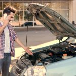 Young handsome man standing near car with open hood and calling