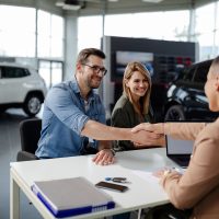 Male customer and female car dealer shaking hands at showroom.