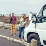 Female mechanic fixing the broken down camper van of a couple going on a trip