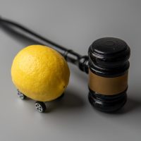 A lemon with wheels and a judge gavel. Lemon law concept.