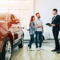 Young modern happy couple buying a new car in city dealership and talking with salesman