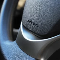 Close-up of a textured car steering wheel with "Airbag" embossed. The design features smooth curves, conveying modernity and safety.