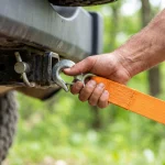 Male hand attaching orange tow strap to vehicle hitch receiver outdoors