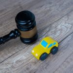 Black wooden gavel lying next to a yellow toy car on a rustic wood floor, a concept image for vehicle accident law.